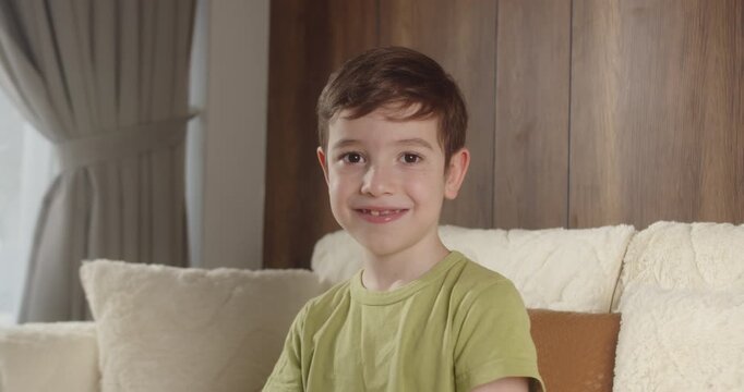 Portrait of smiling 8 year old boy with tooth gap sitting on sofa at home.