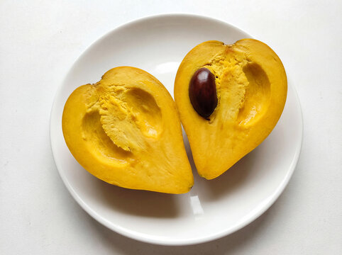 Sliced canistel fruit or eggfruit on white plate, halves of yellow pouteria campechiana isolated on bright background