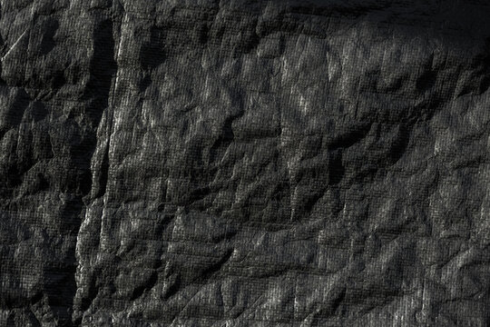 Close-up of a thick black outdoor tarp with a rugged, wrinkled surface. The heavy material shows strong texture, folds, and irregular patterns.
