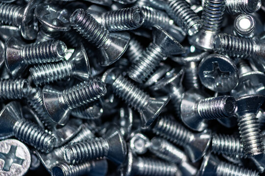 Close-up of numerous shiny galvanized countersunk screws DIN 965, their metallic luster reflecting light. An industrial, hardware background