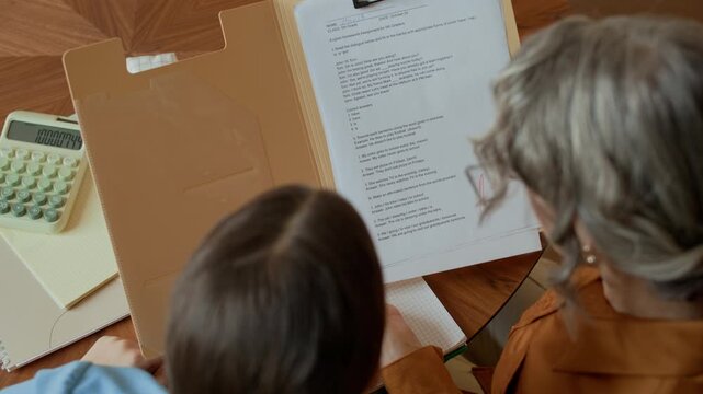 Directly above view of grandmother supporting granddaughter while looking at test result sitting at table in apartment