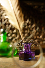 Vintage still life of a antique feather quill in a purple glass inkwell. Set on a rustic wood desk with warm, dramatic lighting. Soft-focus background creates a nostalgic, historical mood. Vertical.