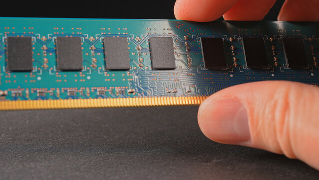 DDR RAM memory chips module macro view. Hand holding Random Access Memory RAM module disconnected from computer motherboard. Manufacturers redirect capacity production for AI data centers processing.