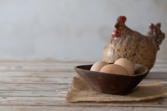 Fresh Brown Eggs in Rustic Wooden Bowl with Ceramic Hen on Distressed Wood with Copy Space