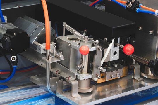 Close-up of industrial automation machinery with metallic components, red knobs, and colorful tubing. Machine parts show precision engineering for manufacturing