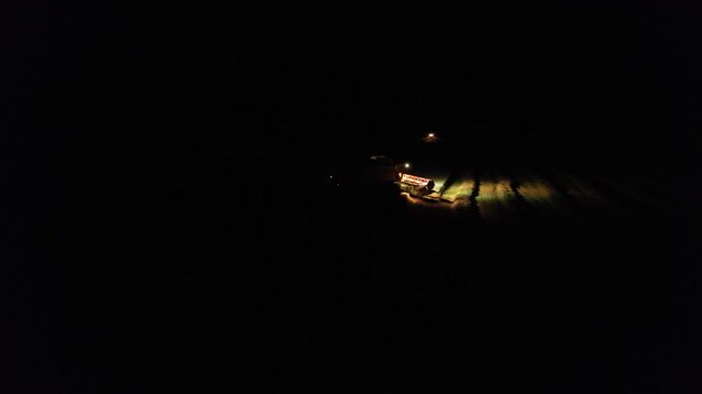 Combine harvesters working on grain field at night with bright lights captured as aerial panorama documenting intensive agricultural harvest with modern machinery