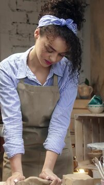 Woman kneading clay with hands while preparing material for pottery. Female artisan pressing and shaping soft material on table. Creating base for ceramic piece. Focusing on texture.