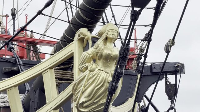 Slow zoom on a frigate figurehead with ropes, cables and pulleys, revealing bow rigging details and traditional fittings of a classic sailing ship in maritime setting