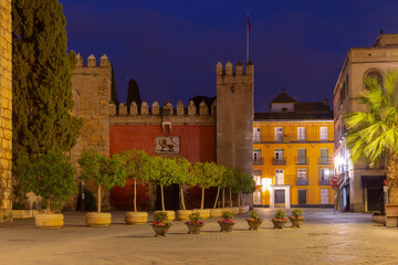 Night view of Puerta del Leon entrance with illuminated walls and historic buildings at the Alcazar of Seville, Spain.