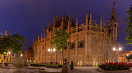 Night view of Seville Cathedral illuminated with street lamps and historic architecture in Seville, Spain.