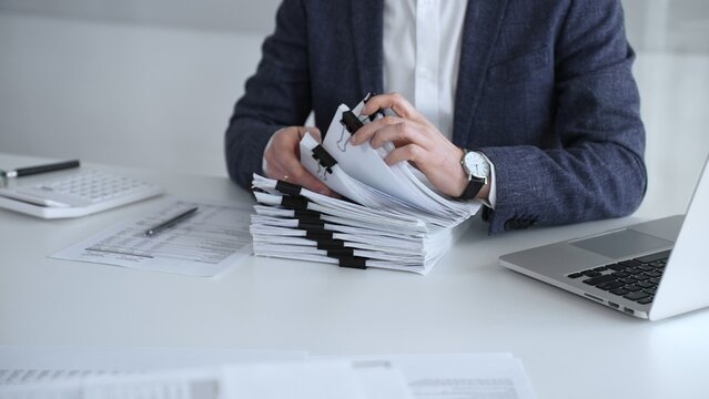 Business professional organizing documents at desk, managing paperwork and financial reports, working on taxes or corporate accounts with a laptop and calculator for audit preparation. Audit and taxes