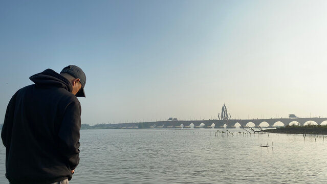 Man standing by serene water with bridge in background