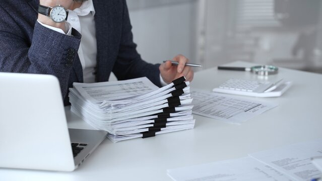 Financial professional working on tax documents, calculating data, and reviewing paperwork at a modern office desk, managing important business finance records and auditing reports. Audit and taxes