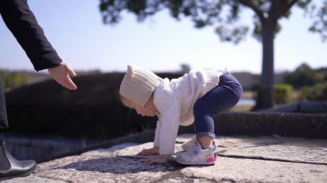 Little child crawls on stone path. Child reaches out, curious and playful. Adult guides child with gentle hand. Warm sunlight bathes the scene. Child learns to walk with trust and joy