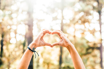 Woman hands making heart shape in forest expressing love for nature and environment. Close up outdoor detail with green background, sustainability concept and peaceful leisure lifestyle