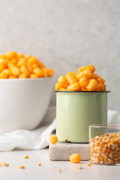 cheese puff snacks in a green cup on a white countertop, crispy cheese balls made of cornmeal in a green enamel cup on a white background