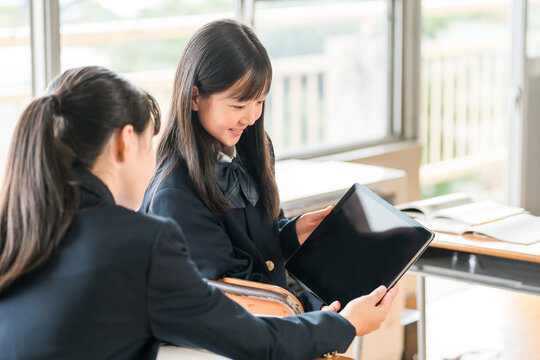Female middle and high school students in their school uniforms studying using tablets.