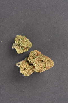Three dried cannabis buds with green and orange hues placed on a dark textured surface.
