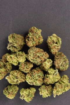 Close-up image of multiple cannabis buds arranged on a dark surface, showcasing their green and orange hues with visible trichomes.