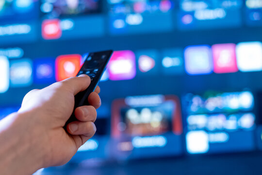 Close-Up Hand Gripping TV Remote with Streaming Apps on Screen