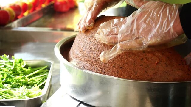 Chef hands in gloves kneading cig kofte in steel tray, preparing traditional turkish food.