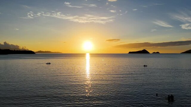 Amanecer dorado en playa tropical de Costa Rica con siluetas de botes y ba&ntilde;istas, toma a&eacute;rea de drone.