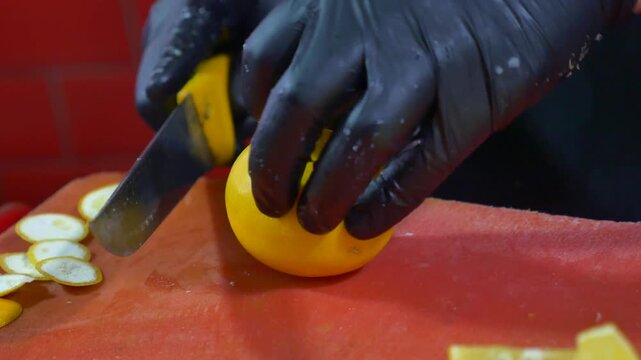 Professional chef cutting fresh lemons on red board with sharp knife in commercial kitchen.