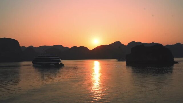 Sunset over Ha Long Bay with boat silhouette and reflection