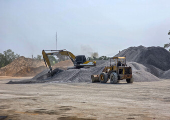 A hydraulic excavator and a wheel loader working together on large stockpiles of crushed stone at an industrial construction site.   © wannasak