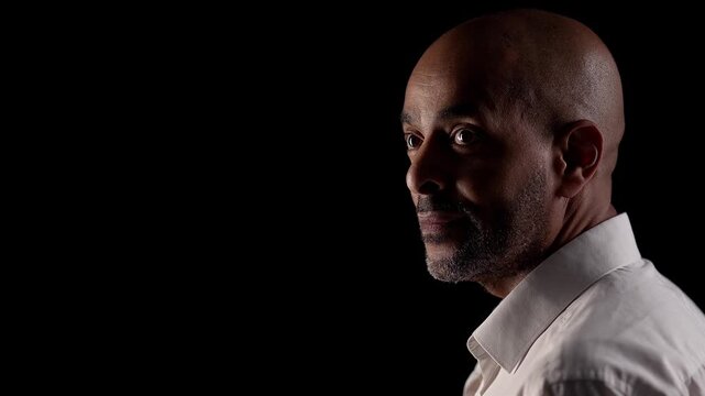 Illustrating mental health awareness A middle-aged man is seen in profile against a black background looking thoughtful and serious in a studio setting.