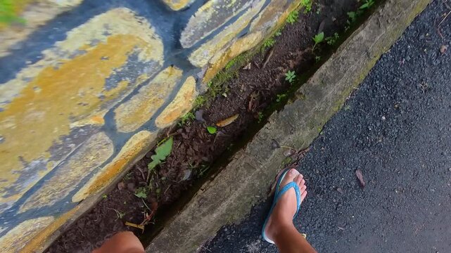 Overhead clip of a man digging a drain with a hoe and pouring the soil into a bucket. Video of a man cleaning a house gutter of weeds and dirt. First-person POV footage with steady 4K resolution.