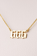 Close-up of a gold pendant with the number 666 on a chain, set against a luxurious white leather background.