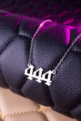 Close-up of a silver pendant with the number 444 on a chain, set against a luxurious black leather background.