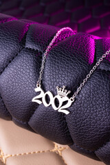 Close-up of a silver pendant with the year 2002 and a cute crown on a chain, set against a luxurious black leather background.