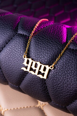 Close-up of a gold pendant with the number 999 on a chain, set against a luxurious black leather background.