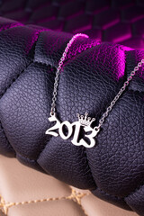 Close-up of a silver pendant with the year 2013 and a cute crown on a chain, set against a luxurious black leather background.