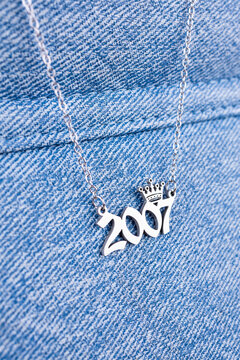 Close-up of a silver pendant featuring the year 2007 and a cute crown on a chain, set against a blue background.