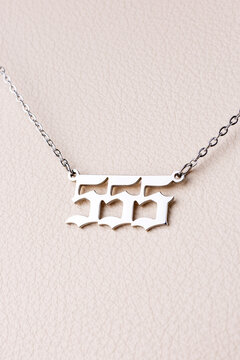 Close-up of a silver pendant with the number 555 on a chain, set against a luxurious white leather background.