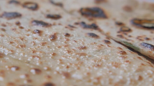 Macro camera movement over crispy toasted flatbread texture with brown charred spot detail.