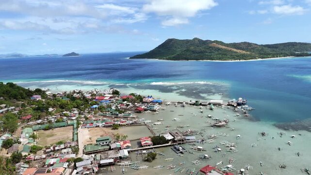 Panning drone shot of San Miguel coastal community in Linapacan with blue ocean and nearby Patoyo Island visible, Philippines