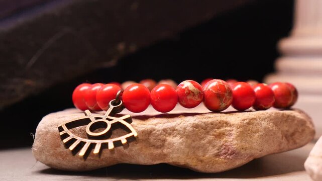 A handmade red beaded bracelet with evil eye charm on a rock in slow motion.