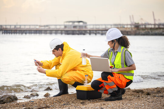 Environmental engineers in protective gear taking water samples near a shipping port, Scientists in hazmat suit conducting coastal water quality research, researchers analyzing sea water pollution