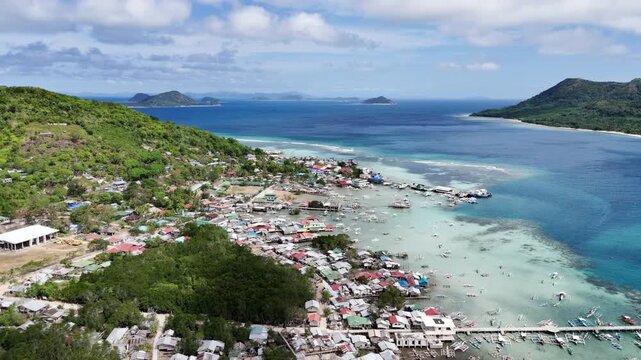 Flyover drone shot of Linapacan proper showing a coastal community beside turquoise waters with Patoyo Island ahead, Philippines