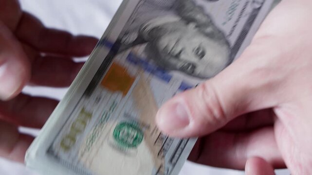 Two hands actively handle a stack of paper currency in an indoor setting. Abstract background enhances focus on financial transaction and value.