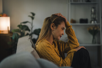 Stressed woman sitting on a sofa at home holding her head while feeling depressed and lonely © PRIME STOCK LAB