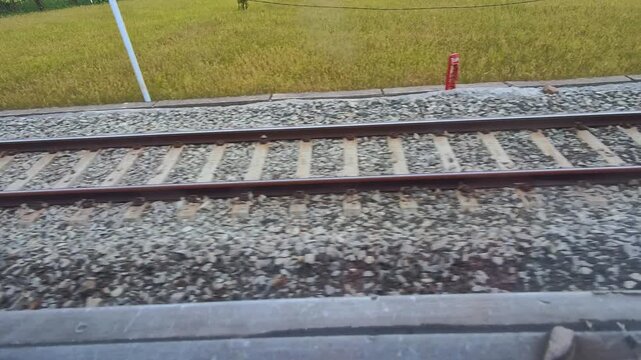 Video of a view of a rusty train track with gravel and rail sleepers from the POV of a passenger sitting on a moving train. Footage of the track for the train's wheels to run steadily, safely, and eff