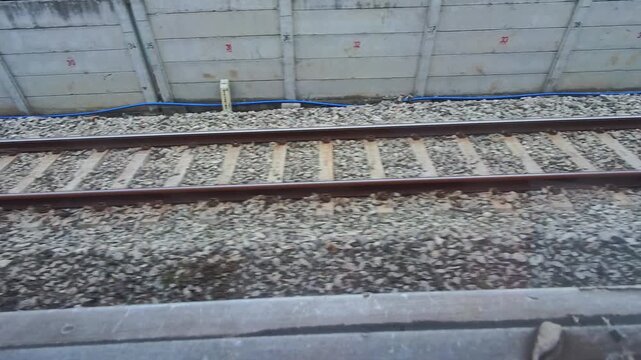 Video of a view of a rusty train track with gravel and rail sleepers from the POV of a passenger sitting on a moving train. Footage of the track for the train's wheels to run steadily, safely, and eff
