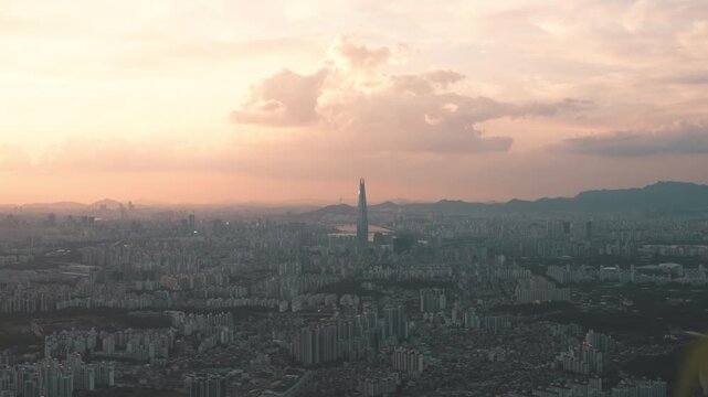 황금빛 일몰 노을 아래 우뚝 솟은 서울 롯데월드타워와 대도시 전경 타임랩스 (Sunset time-lapse of Lotte World Tower and Seoul cityscape under a golden sky)