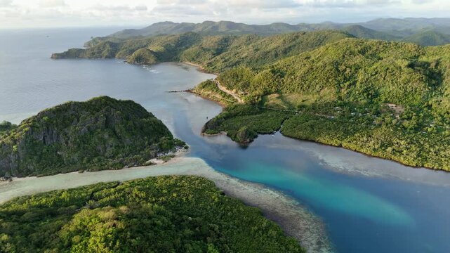 Push-in aerial shot over Linapacan Island highlighting a deep narrow channel cutting through vibrant blue waters and mountainous coastal terrain in the early morning, Philippines