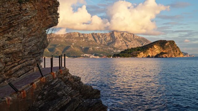 waves gently washing against the shore next to a scenic coastal walkway under a dramatic sky.